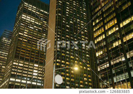 Multiple modern skyscrapers rise closely together in Midtown Manhattan, their windows glowing with artificial light. The night scene reflects the non-stop energy of New York City's business district. Multiple modern skyscrapers rise closely together in Midtown Manhattan, their windows glowing with artificial light. The night scene reflects the non-stop energy of New York City's business district. 126883885