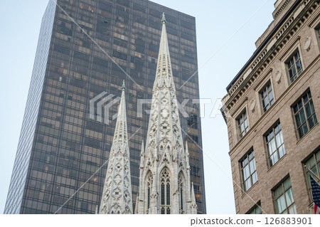 The elegant spires of St. Patrick's Cathedral rise prominently against the glass facade of a modern skyscraper. This iconic contrast captures the architectural diversity of Midtown Manhattan, New York 126883901