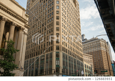 A large brick building with modern glass windows meets neoclassical architecture at a busy corner. The scene shows a contrast of historical and contemporary styles in Manhattan. 126883931