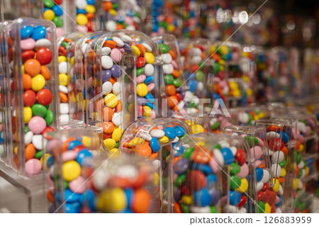 Bright multi-colored candies are packed into transparent letter-shaped containers. The close-up view shows a vibrant candy display in a retail or gift store. Bright multi-colored candies are packed into transparent letter-shaped containers. The close-up view shows a vibrant candy display in a retail or gift store. 126883959