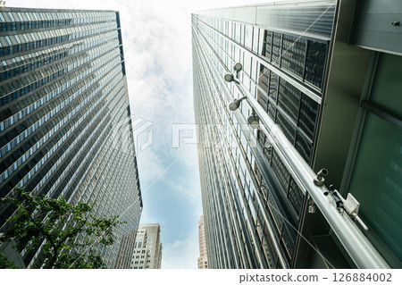 Two sleek skyscrapers stretch into the sky between narrow streets in Midtown Manhattan. A streetlight and security cameras are visible in the foreground, adding a sense of urban infrastructure. Two sleek skyscrapers stretch into the sky between narrow streets in Midtown Manhattan. A streetlight and security cameras are visible in the foreground, adding a sense of urban infrastructure. 126884002