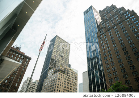 An American flag rises in front of towering buildings in Midtown Manhattan. Glass, brick, and stone architecture represents the city's diverse style. An American flag rises in front of towering buildings in Midtown Manhattan. Glass, brick, and stone architecture represents the city's diverse style. 126884003