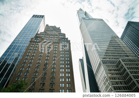 Massive New York skyscrapers tower into a cloudy sky in the heart of Manhattan. Office windows reflect light as the financial core stretches upward. 126884005
