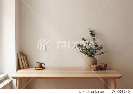 Autumn interior still life. Vase with eucalyptus, olive tree branches, pumpkins. Cup of tea, coffee, books. Wooden table at window. Home office. Minimal Scandi interior. Empty white wall background. Autumn interior still life. Vase with eucalyptus, olive tree branches, pumpkins. Cup of tea, coffee, books. Wooden table at window. Home office. Minimal Scandi interior. Empty white wall background. 126884950