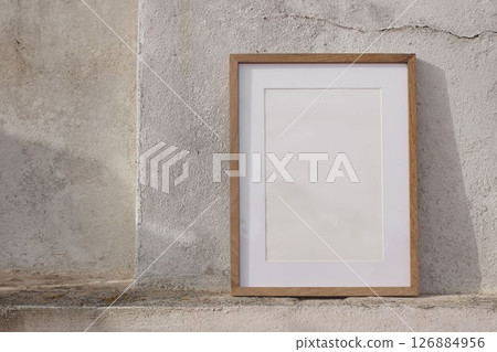 Blank thin wooden picture frame leaning against white textured wall in sunlight. Mininal elegant poster mockup. Artistic template. Natural light, soft shadows. Minimalist summer outdoor scene. A3, A2 Blank thin wooden picture frame leaning against white textured wall in sunlight. Mininal elegant poster mockup. Artistic template. Natural light, soft shadows. Minimalist summer outdoor scene. A3, A2 126884956