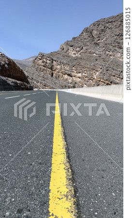 Mountain road curves sharply toward rocky tunnel, mountain road lined with cracked stripe invites passage through rugged layers, contrast between built path and raw cliffs evokes timeless tension. Mountain road curves sharply toward rocky tunnel, mountain road lined with cracked stripe invites passage through rugged layers, contrast between built path and raw cliffs evokes timeless tension. 126885015