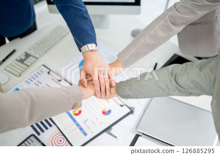 Top view of businessman and woman or office workers joining hands over table with scattered document Top view of businessman and woman or office workers joining hands over table with scattered document 126885295