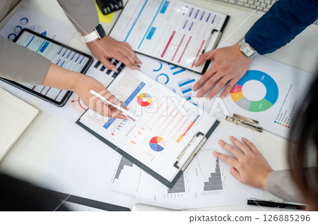 Top view of a hand holding stylus pointing at a clipboard over scattered documents on working desk. 126885296