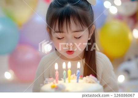 A little girl with long hair blows out candles on a birthday cake. Balloons are hung around it. The concept of advertising is related to holidays, childhood and family moments. Children's emotions 126886067