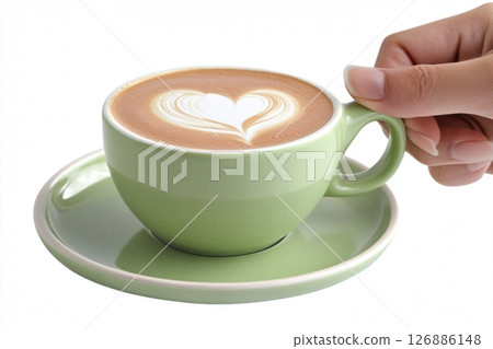 Close-up of a hand holding a pastel green cup with a heart-shaped latte art on top. Elegant presentation on matching saucer, isolated on white. Ideal for cafe, morning, or lifestyle concepts 126886148