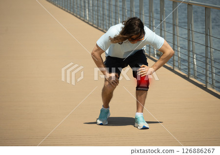 Sudden knee pain in athlete while jogging. Athlete bodybuilder leg wearing knee support brace or elastic kneecap bandage. Health problems and pain. 126886267