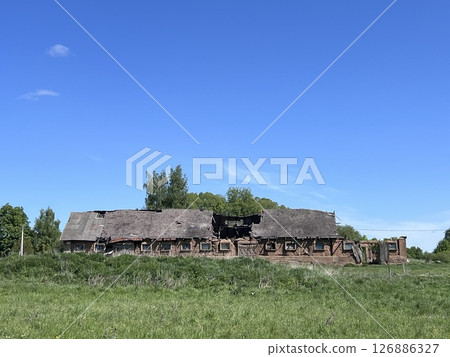 View on cattle or pig farm in abandoned village in Lithuania. Landscape with field, buildings, blue sky and clouds in sunny day. View on cattle or pig farm in abandoned village in Lithuania. Landscape with field, buildings, blue sky and clouds in sunny day. 126886327