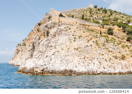 Rocky coast with an ancient stone fortress wall stretching along the top of the hill. Blue sky, azure sea and picturesque Mediterranean landscape. Seaside resort trip.Turkey Rocky coast with an ancient stone fortress wall stretching along the top of the hill. Blue sky, azure sea and picturesque Mediterranean landscape. Seaside resort trip.Turkey 126886414