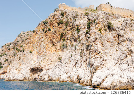 Rocky coast with an ancient stone fortress wall stretching along the top of the hill. Blue sky, azure sea and picturesque Mediterranean landscape. Seaside resort trip.Turkey 126886415