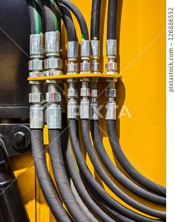 Detailed view of hydraulic hoses and connectors in heavy machinery at a construction site during daytime 126886552