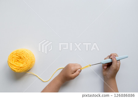 Child crocheting with yellow yarn and hook on white background 126886886