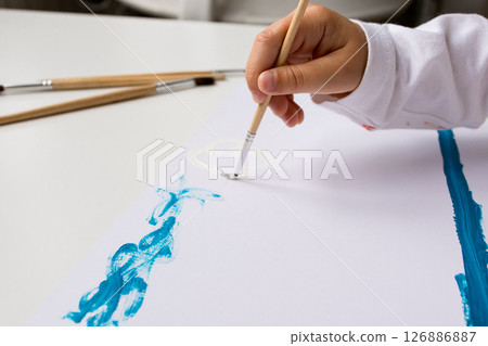 Child painting with brush on white canvas 126886887