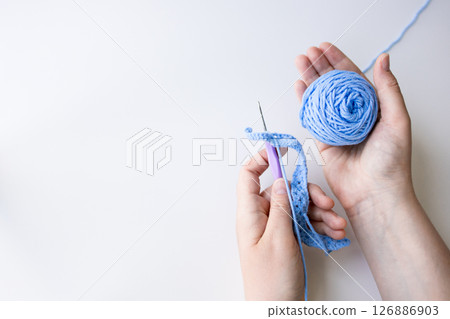 Hands crafting with blue yarn and crochet hook on white background 126886903