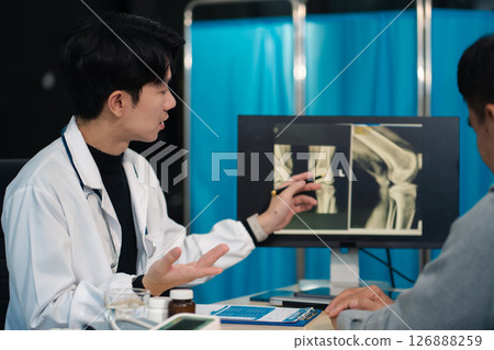 Male doctor explains knee osteoarthritis and arthroplasty treatment after x-ray. 126888259