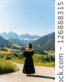 Visit Italy. Early sun spills over a woman in an elegant black dress, lost in the vastness of alpine fields and mountain silence, a serene call to the Dolomites 126888315