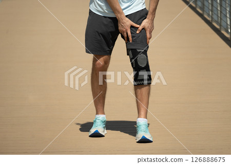Man putting knee brace to support painful leg. Athlete bodybuilder leg wearing knee support brace or elastic kneecap bandage. Sleeve for compression. Health problems and pain. 126888675