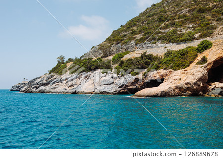 Sea cave in a rocky shore with turquoise transparent water. Picturesque natural landscape with rough texture of stones and deep entrance to the grotto. Ecotourism. Fascinating seascape. 126889678