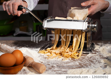 Caucasian female hands making fettuccine noodles using mechanical pasta machine Caucasian female hands making fettuccine noodles using mechanical pasta machine 126889892