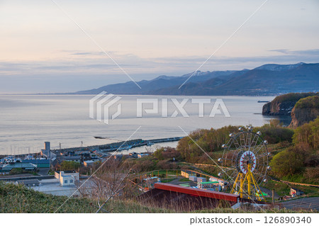 An amusement park with a Ferris wheel by the sea bathed in the morning sun An amusement park with a Ferris wheel by the sea bathed in the morning sun 126890340