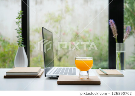 Side view of a laptop with orange juice cup and notebooks, working by the window 126890762