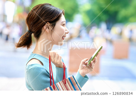 A stylish young woman operating a smartphone while shopping A stylish young woman operating a smartphone while shopping 126890834