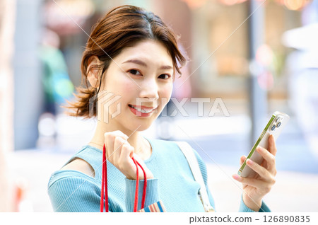 A stylish young woman operating a smartphone while shopping A stylish young woman operating a smartphone while shopping 126890835