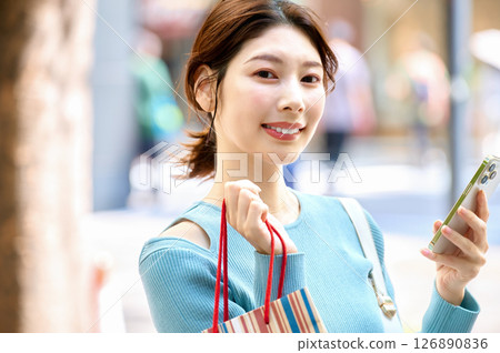 A stylish young woman operating a smartphone while shopping 126890836