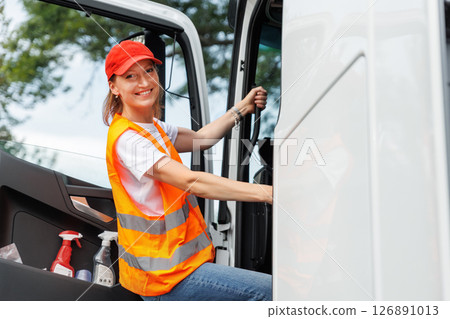 Portrait young adult happy smiling woman climbing cabin heavy truck driver cargo vehicle. Female person girl professional job career working driving freight engine lorry. Logistics industry 126891013