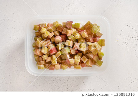 Freshly chopped frozen rhubarb prepared in plastic box on white background. Trendy organic food. View from above. 126891316