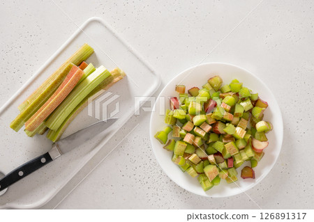 Freshly chopped green rhubarb in white plate on white background. Trendy organic food. Ready for cooking. Vegan concept. View from above. 126891317