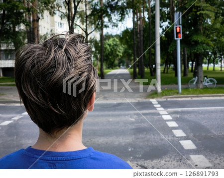 a child at a pedestrian crossing rear view. Rear view shot of a schoolboy waiting at red traffic light a child at a pedestrian crossing rear view. Rear view shot of a schoolboy waiting at red traffic light 126891793