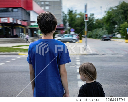 Two brothers, children at a pedestrian crossing rear view. Rear view shot of a schoolboy waiting at red traffic light Two brothers, children at a pedestrian crossing rear view. Rear view shot of a schoolboy waiting at red traffic light 126891794