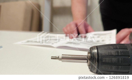 cordless screwdriver or screwdriver. Furniture assembly process. man reads the instructions for assembling furniture cordless screwdriver or screwdriver. Furniture assembly process. man reads the instructions for assembling furniture 126891819