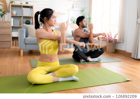 Young asian couple practicing yoga in living room at home, stretching arm pose. Young asian couple practicing yoga in living room at home, stretching arm pose. 126892209