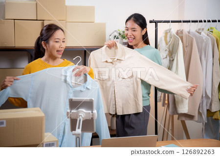 Two young asian woman live online clothing store while showing clothing with tablet on social. Two young asian woman live online clothing store while showing clothing with tablet on social. 126892263