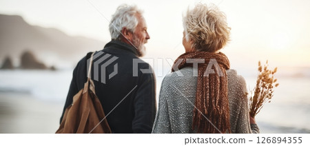 An elderly couple enjoys a romantic stroll on the beach at sunset symbolizing enduring love. 126894355