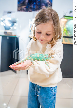 Little girl holding a green chameleon in her hands. Concept of childhood curiosity, interaction with exotic animals, and early interest in biology Little girl holding a green chameleon in her hands. Concept of childhood curiosity, interaction with exotic animals, and early interest in biology 126895128