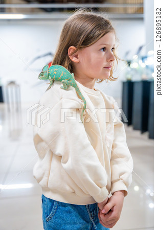 Little girl holding a green chameleon in her hands. Concept of childhood curiosity, interaction with exotic animals, and early interest in biology 126895182