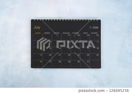 Blank calendar for July 2026, Black spiral desktop calendar on wooden background. 126895256