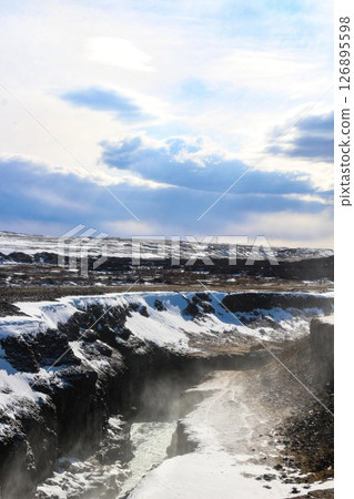 vertical photo took in Gullfoss Falls, Hvita river, Golden Circle, Reykjavik, Iceland. A waterfall cascading over rocky cliffs into a river below with snow covered areas and a clear blue sky vertical photo took in Gullfoss Falls, Hvita river, Golden Circle, Reykjavik, Iceland. A waterfall cascading over rocky cliffs into a river below with snow covered areas and a clear blue sky 126895598