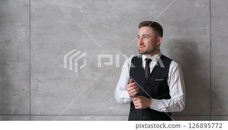man in business clothes stands against wall, adjusting cuffs of his shirt, with a focused look. The neutral background and soft lighting create an atmosphere of professionalism and confidence 126895772