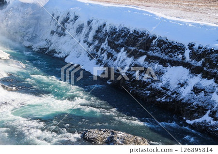 horizontal photo took in Gullfoss Falls, Hvita river, Golden Circle, Reykjavik, Iceland. A waterfall cascading over rocky cliffs into a river below with snow covered areas and a clear blue sky horizontal photo took in Gullfoss Falls, Hvita river, Golden Circle, Reykjavik, Iceland. A waterfall cascading over rocky cliffs into a river below with snow covered areas and a clear blue sky 126895814