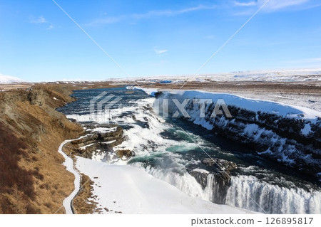 horizontal photo took in Gullfoss Falls, Hvita river, Golden Circle, Reykjavik, Iceland. A waterfall cascading over rocky cliffs into a river below with snow covered areas and a clear blue sky horizontal photo took in Gullfoss Falls, Hvita river, Golden Circle, Reykjavik, Iceland. A waterfall cascading over rocky cliffs into a river below with snow covered areas and a clear blue sky 126895817