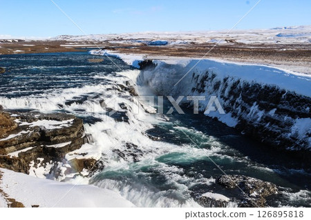 horizontal photo took in Gullfoss Falls, Hvita river, Golden Circle, Reykjavik, Iceland. A waterfall cascading over rocky cliffs into a river below with snow covered areas and a clear blue sky horizontal photo took in Gullfoss Falls, Hvita river, Golden Circle, Reykjavik, Iceland. A waterfall cascading over rocky cliffs into a river below with snow covered areas and a clear blue sky 126895818