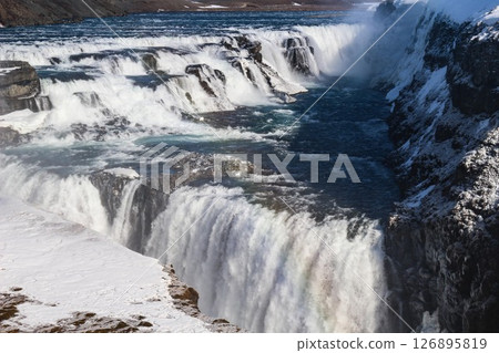 horizontal photo took in Gullfoss Falls, Hvita river, Golden Circle, Reykjavik, Iceland. A waterfall cascading over rocky cliffs into a river below with snow covered areas and a clear blue sky horizontal photo took in Gullfoss Falls, Hvita river, Golden Circle, Reykjavik, Iceland. A waterfall cascading over rocky cliffs into a river below with snow covered areas and a clear blue sky 126895819